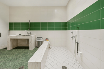 A bathroom with green tiles on the wall and white tiles on the floor.